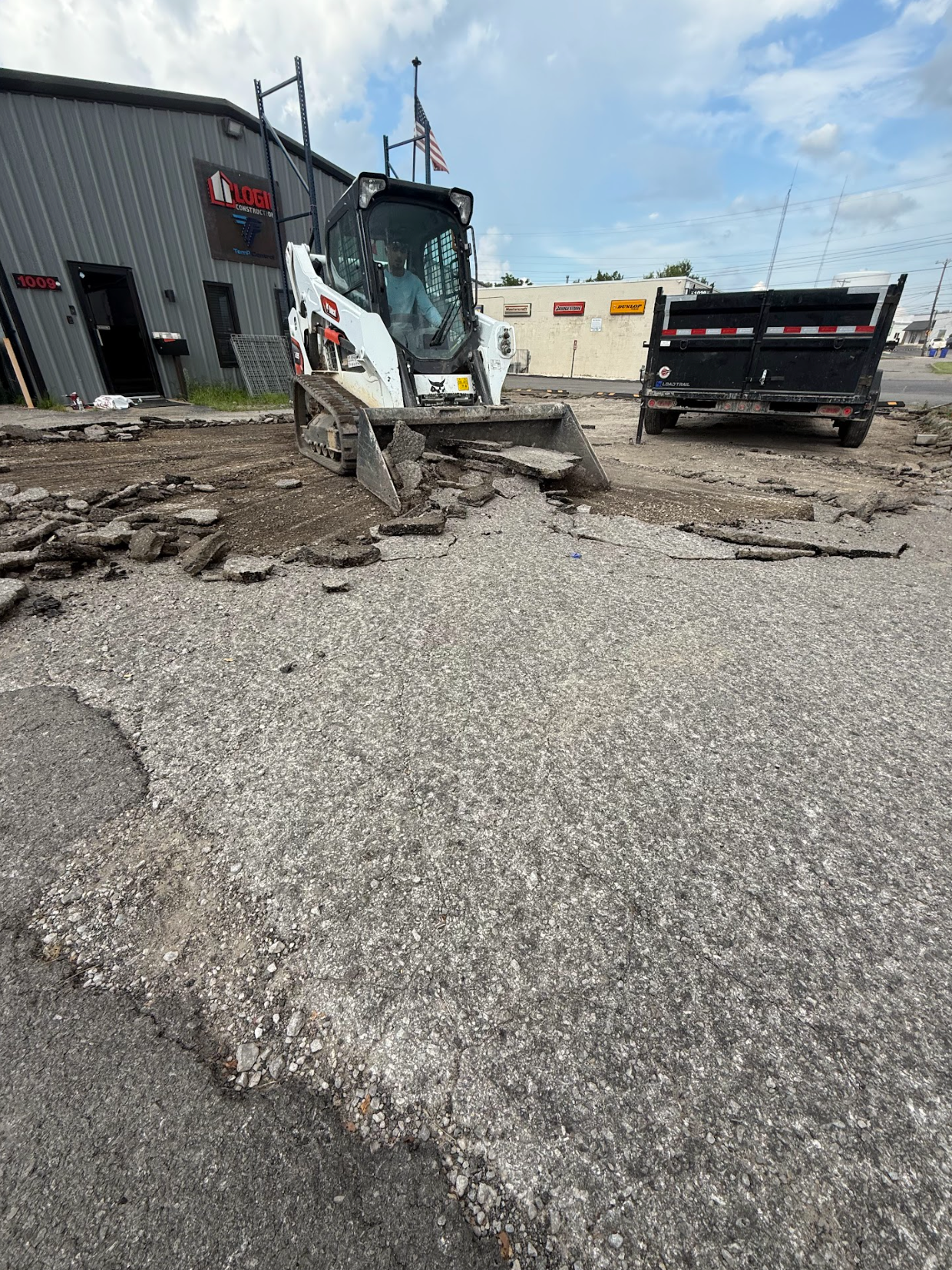 Bobcat skid-steer removing asphalt from a parking lot, with dump truck in background.