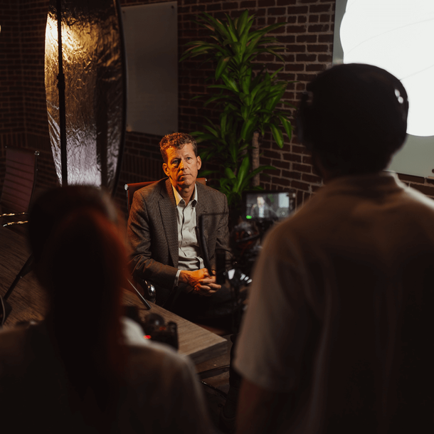 A man is sitting in front of a camera in a room with motorcycles.