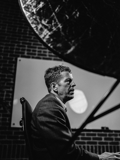 Trace is holding a camera in a field while another man stands behind him.