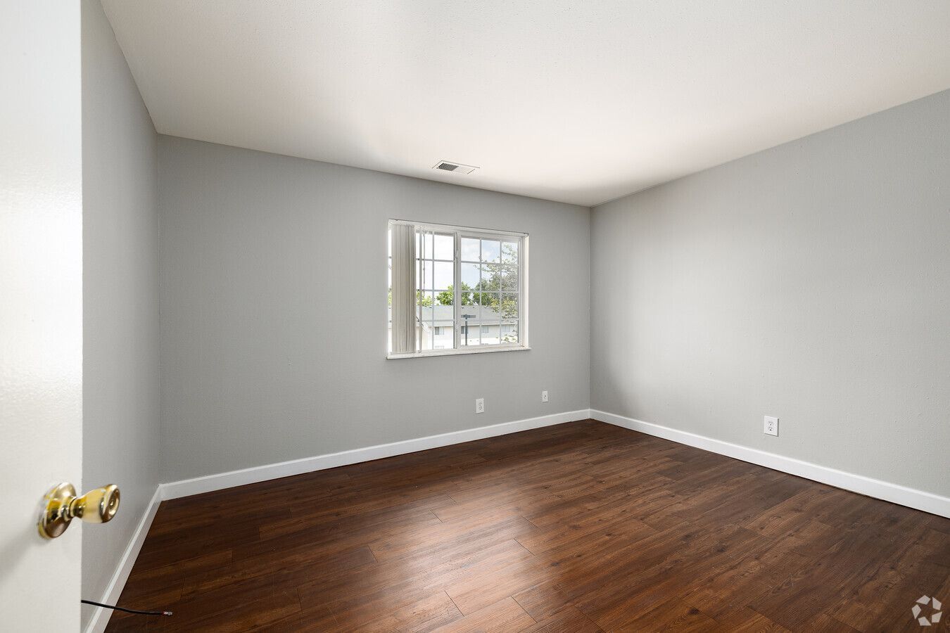 An empty bedroom with hardwood floors and a window.