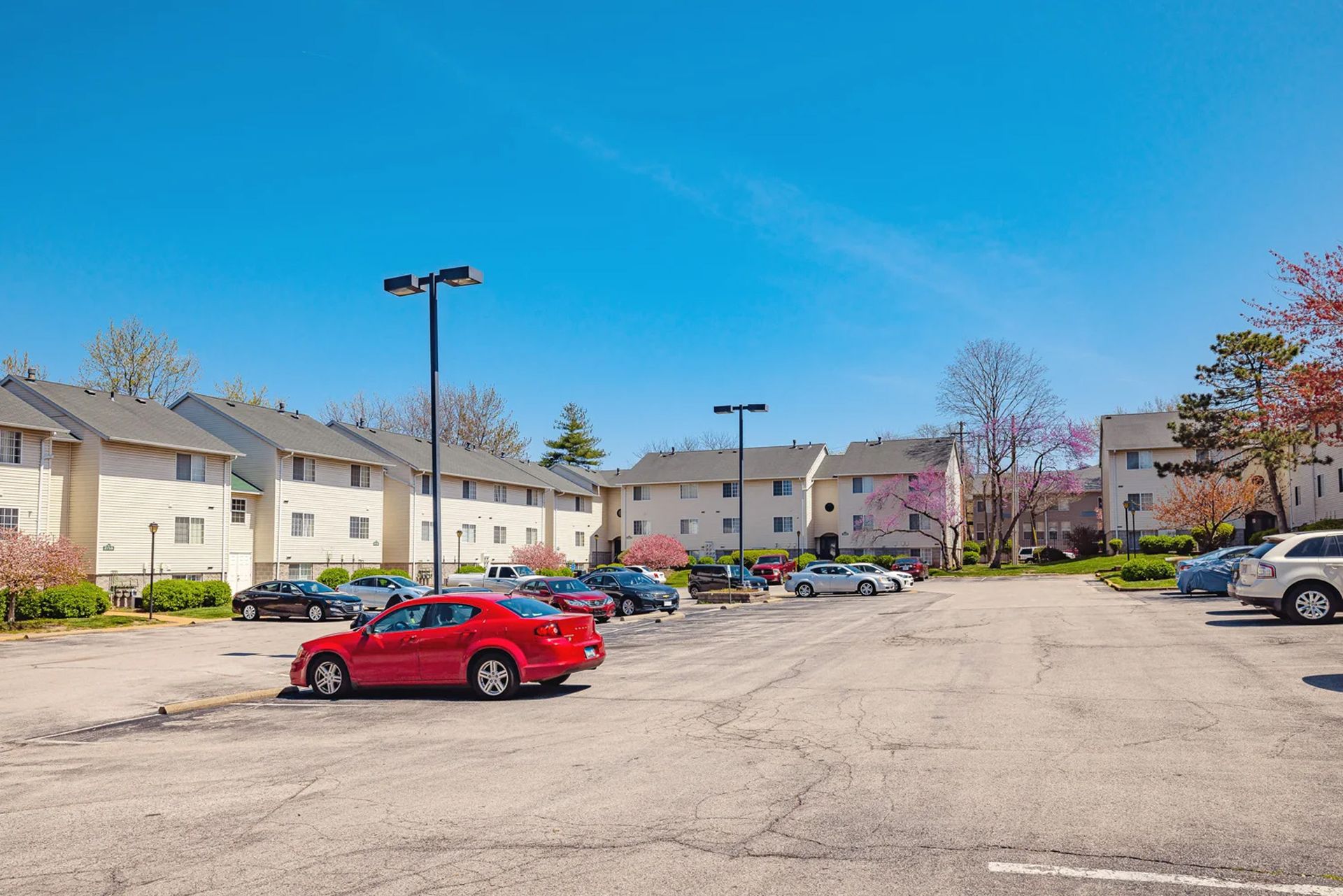 A red car is parked in a parking lot in front of a building.