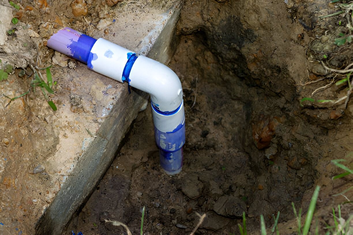 A pvc pipe is sitting in the dirt next to a concrete wall.