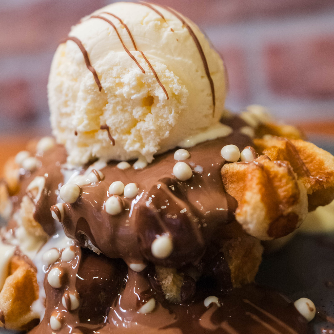 Waffle dessert topped with vanilla ice cream, chocolate sauce, and white chocolate pearls.