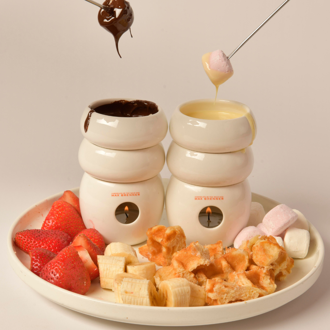 Chocolate and cheese fondue set with strawberries, bananas, waffles, and marshmallows. Two forks dipping into each fondue pot.