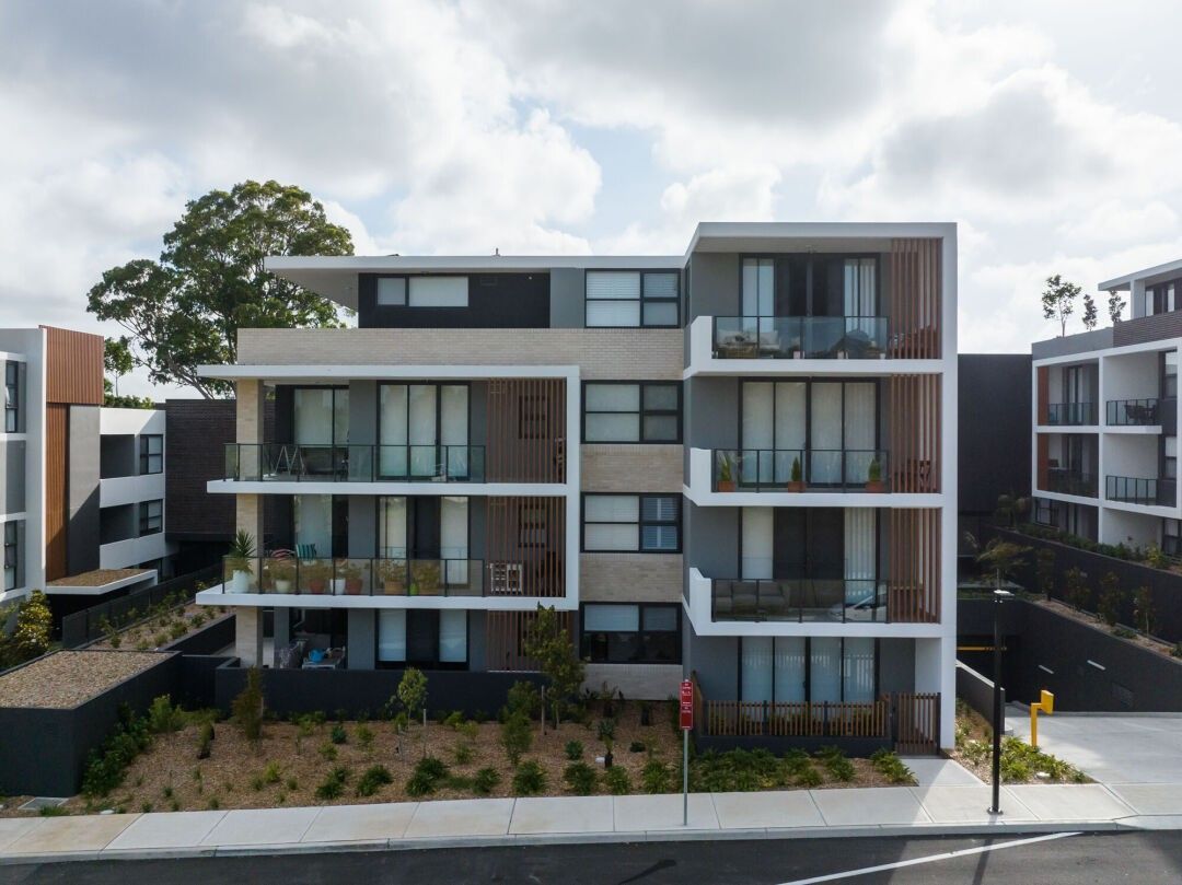 Modern apartment building with balconies, surrounded by trees and other similar structures on a sunny day.