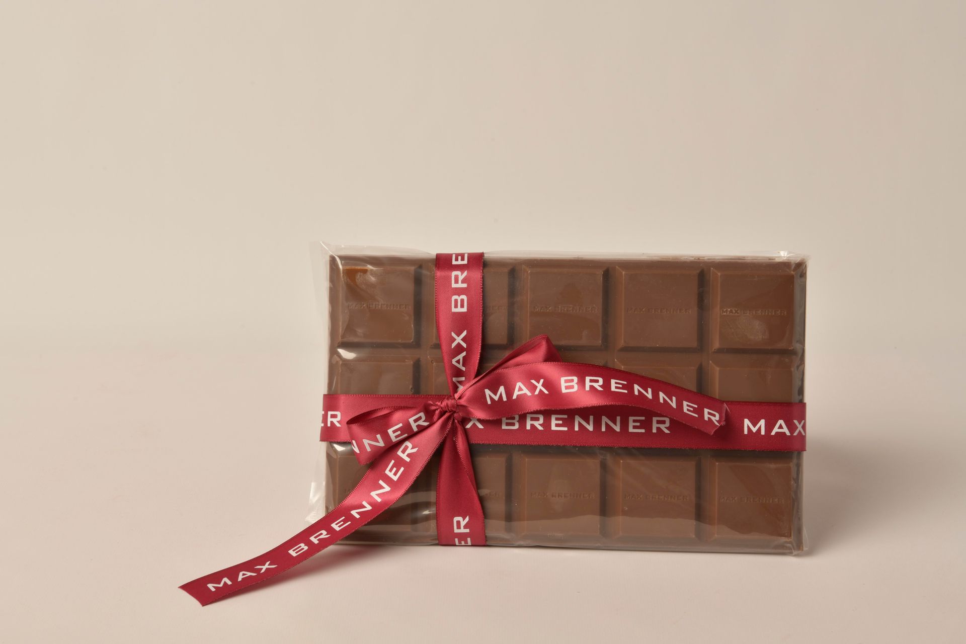 Max Brenner chocolate bar wrapped in clear plastic and tied with a red ribbon.