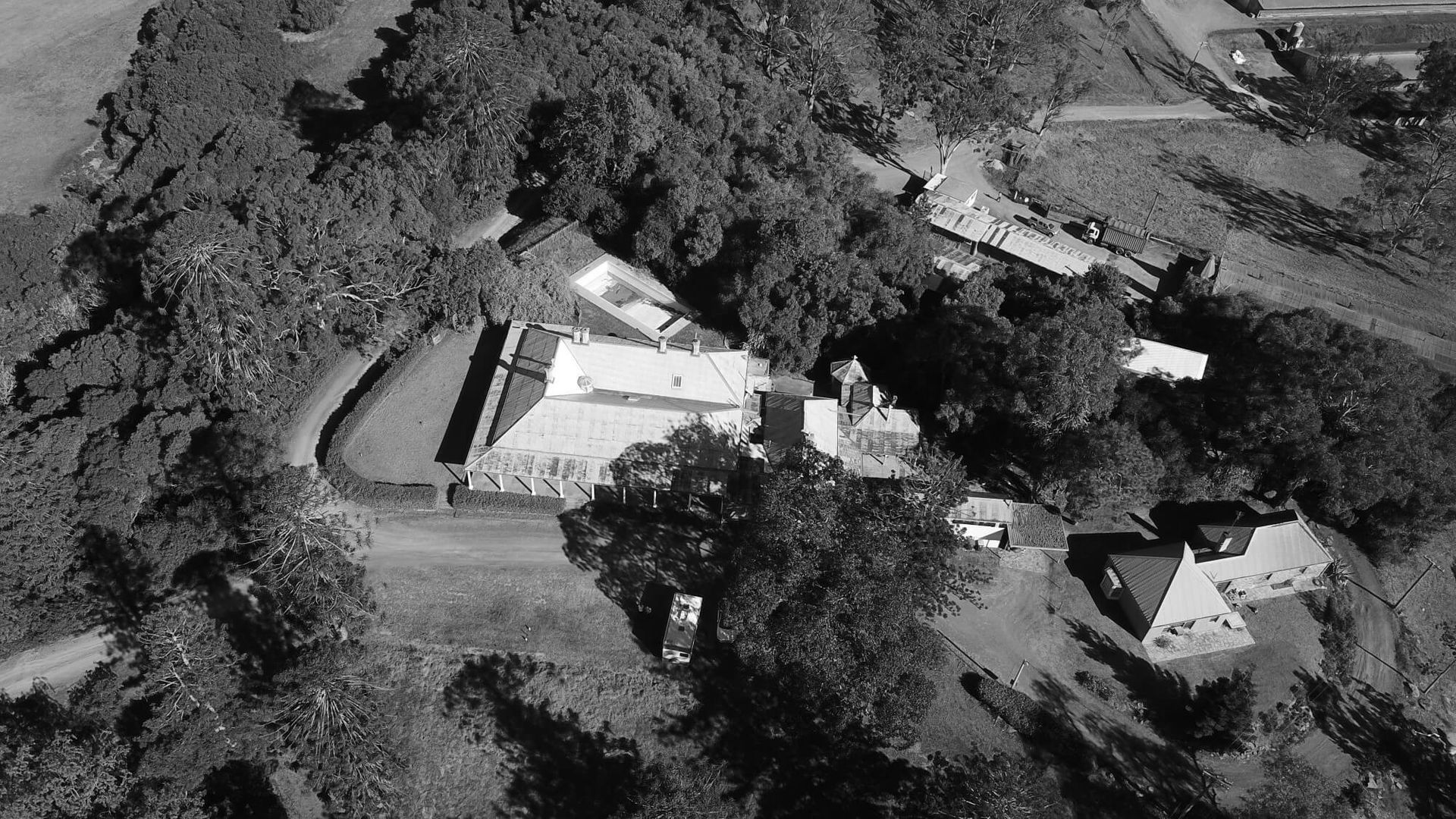 Aerial view of a white building surrounded by trees, with a road curving through the scene.