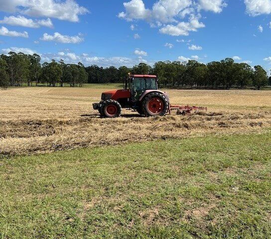 Tractor in a field, pulling a rake. Red and orange tractor on a sunny day, blue sky with clouds.