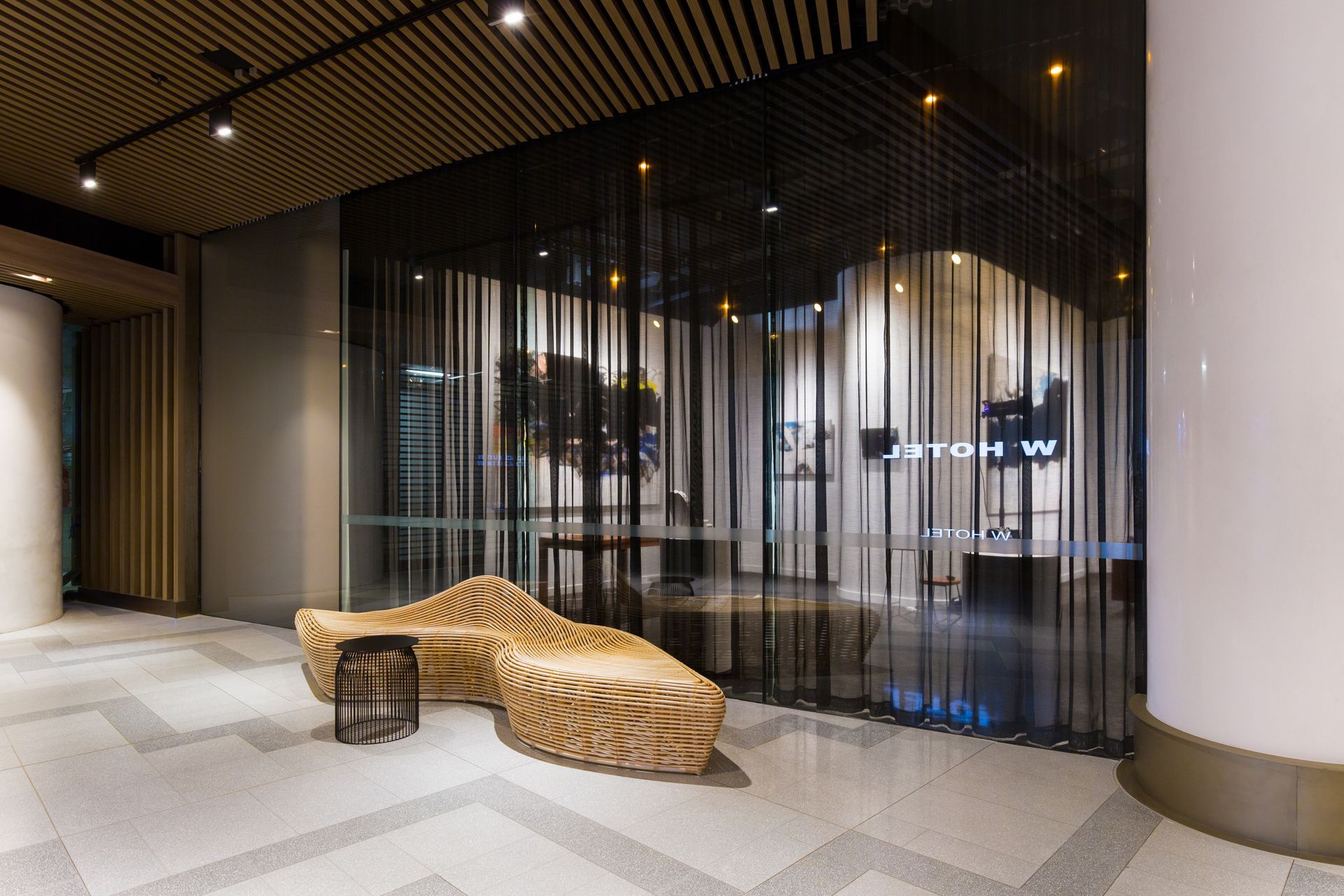 A lobby with a wicker chair and a table in front of a glass wall.