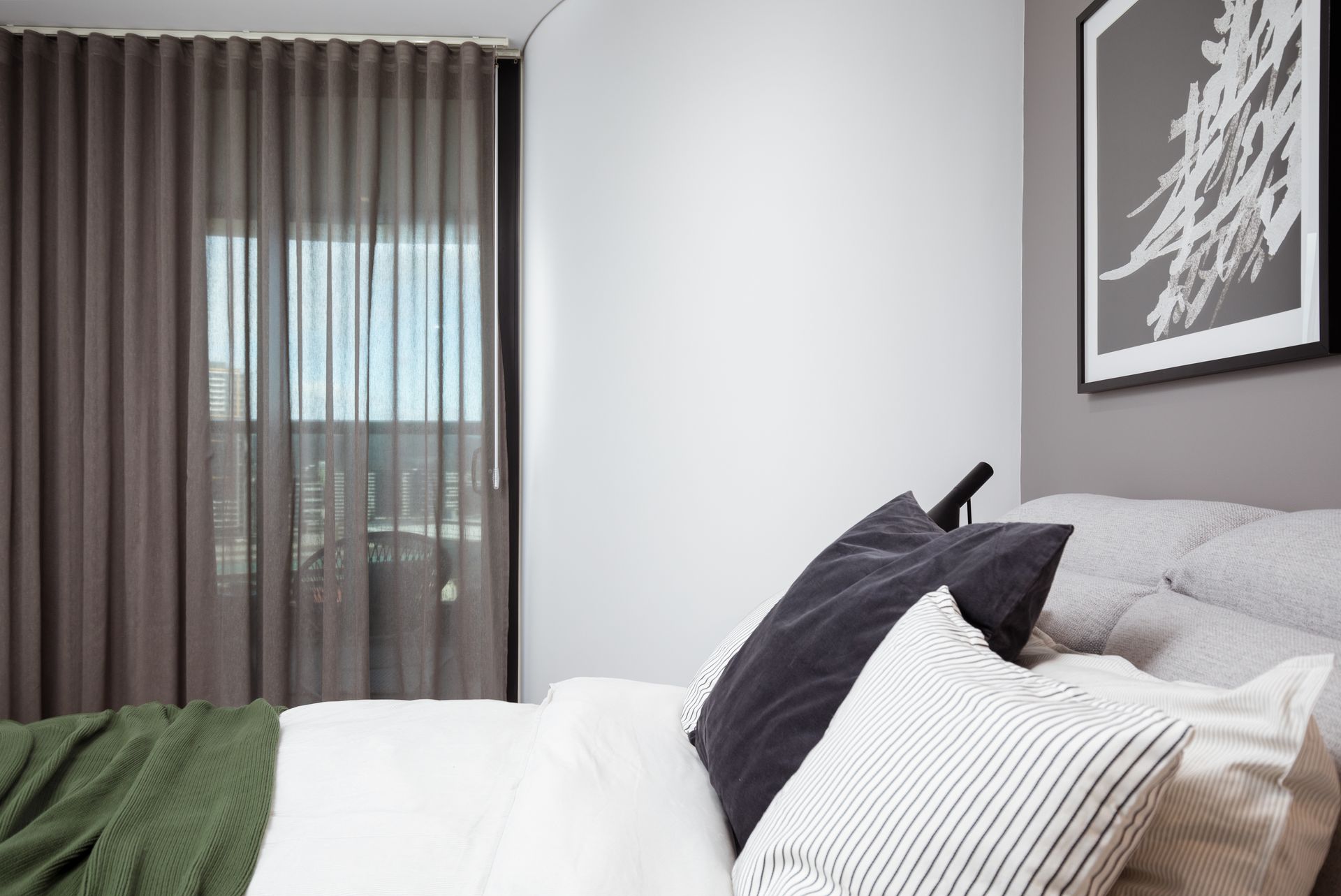 A bedroom with a bed , pillows , curtains and a picture on the wall.