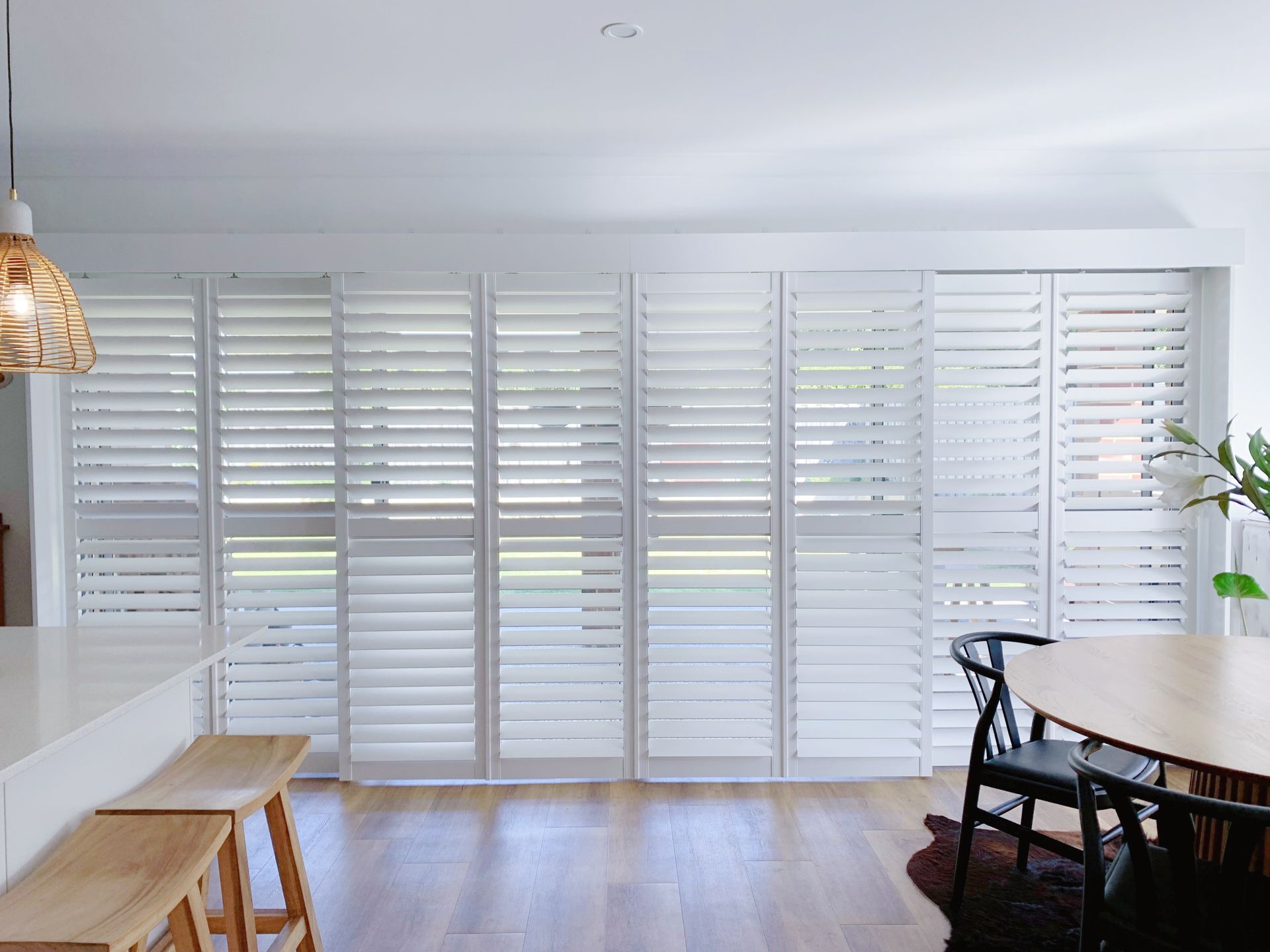 A dining room with a table and chairs and white shutters on the windows.