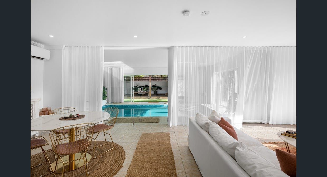 A living room with a couch , table and chairs and a pool in the background.