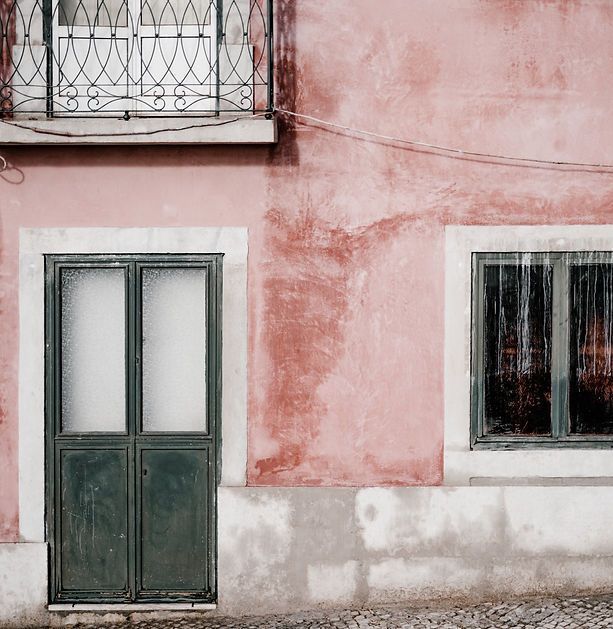 Um prédio rosa com uma porta verde e duas janelas