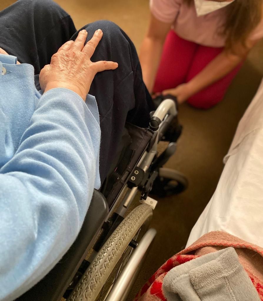 Uma senhora idosa em uma cadeira de rodas com uma criança ajoelhada ao lado dela