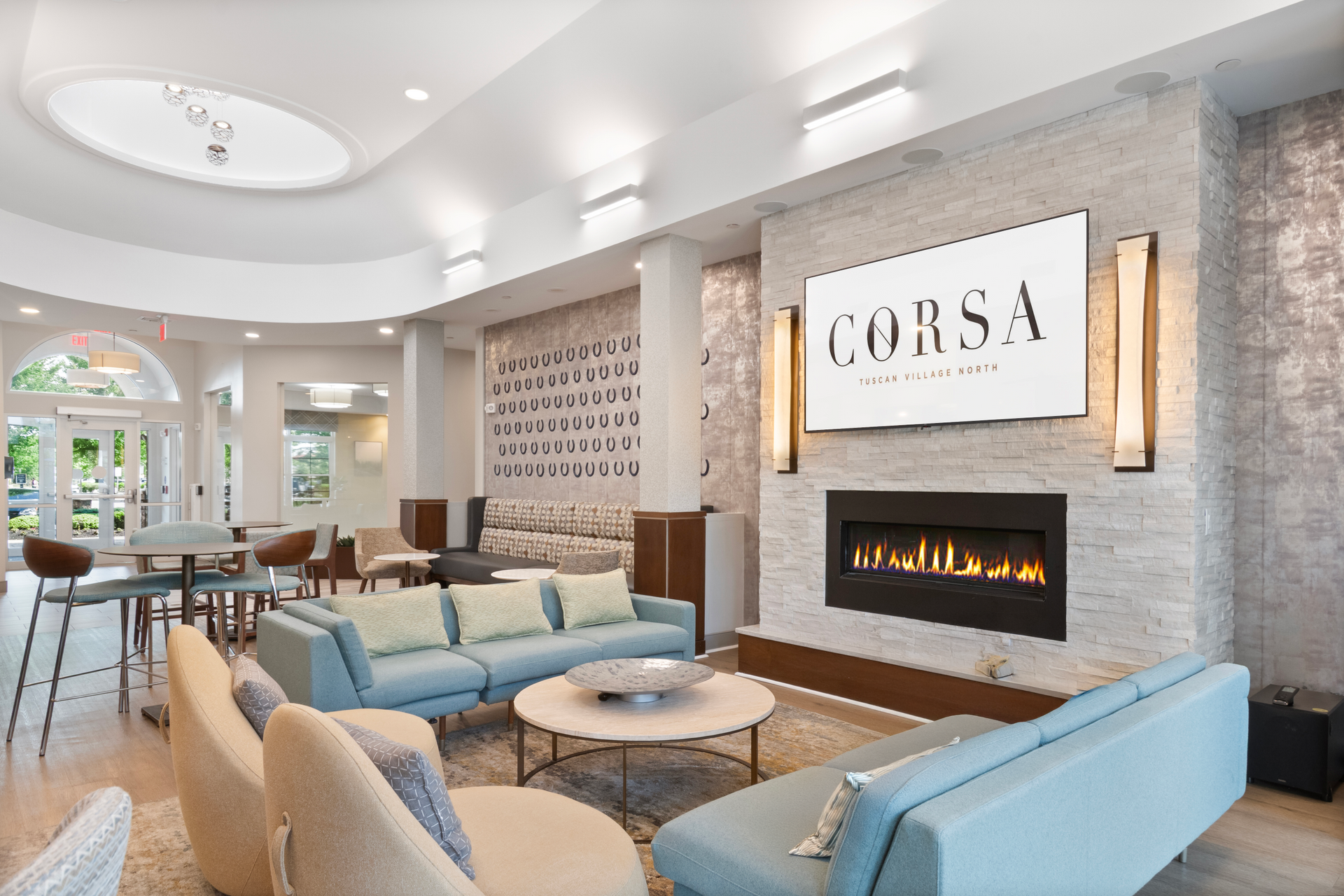 Bright modern lounge with blue chairs, fireplace, and a large “CORSA” wall sign at Corsa Tuscan Village in Salem, NH.