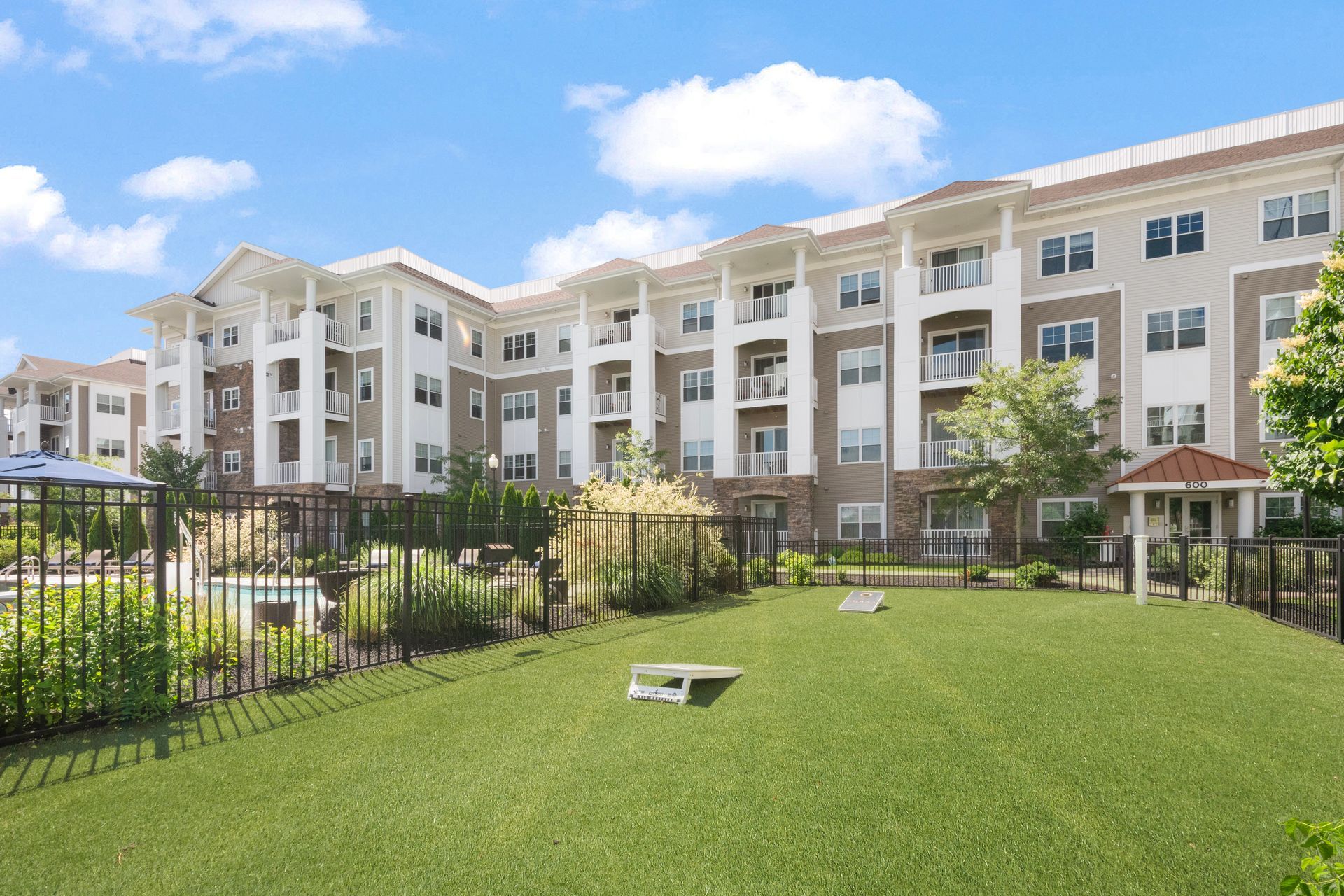 Apartment complex with white balconies, black fence, and green lawn under a blue sky at Corsa Tuscan Village in Salem, NH.