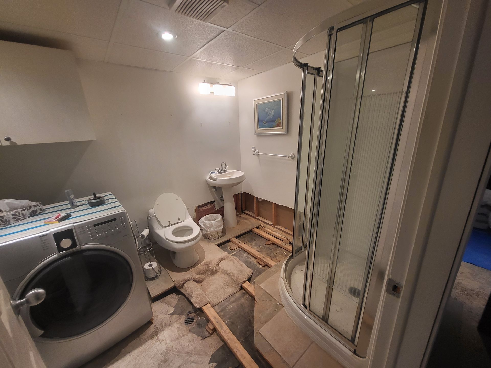 Une salle de bain avec machine à laver, WC, lavabo et douche.