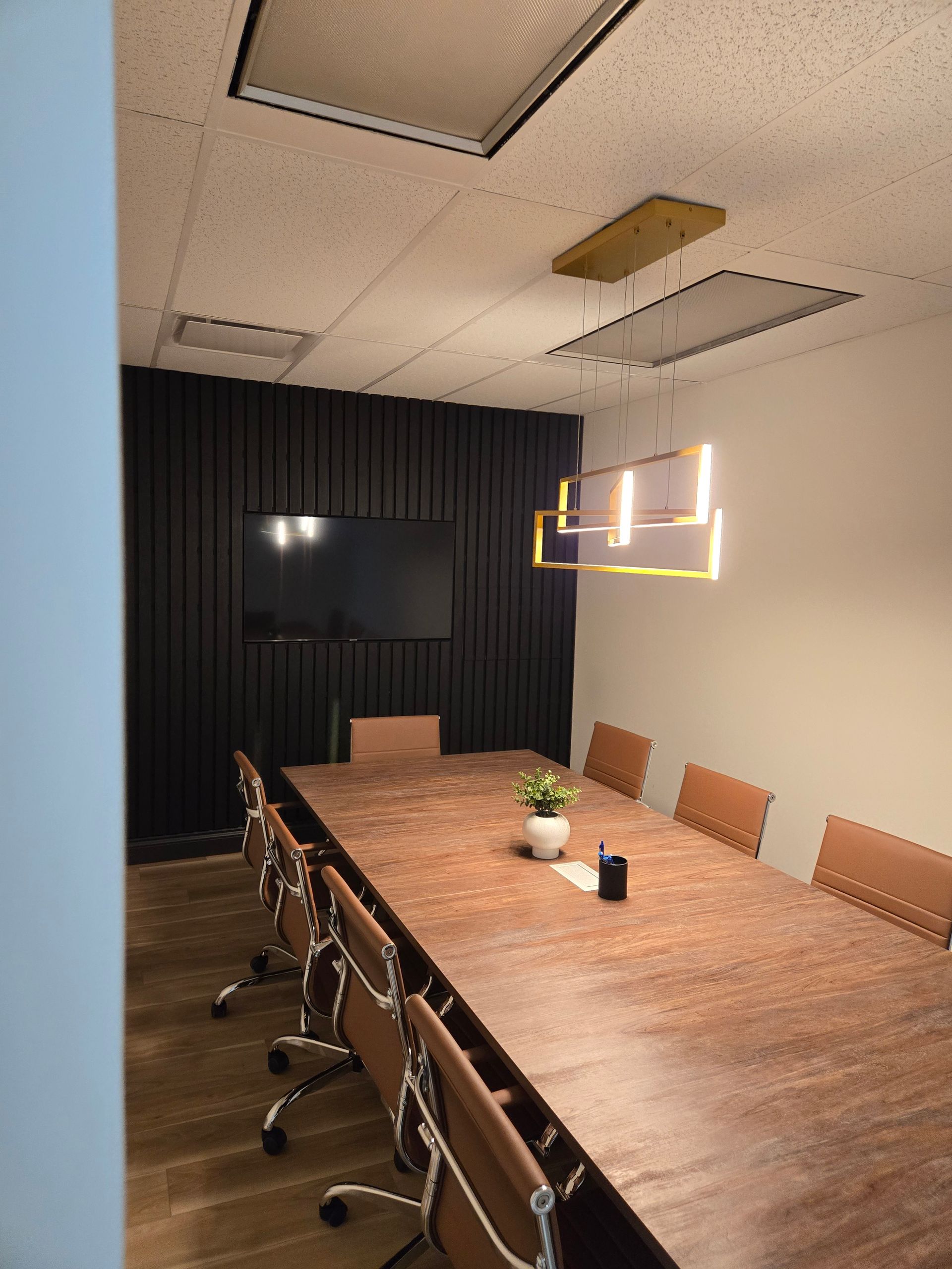 Une salle de conférence avec une longue table et des chaises en bois et une télévision à écran plat.