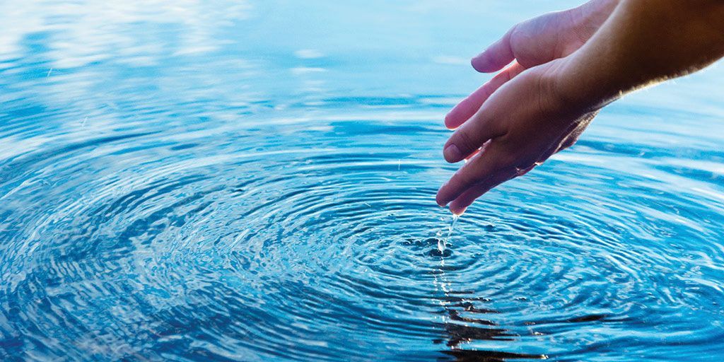 Hands cupped over water, with a single drop falling into concentric ripples in the water.