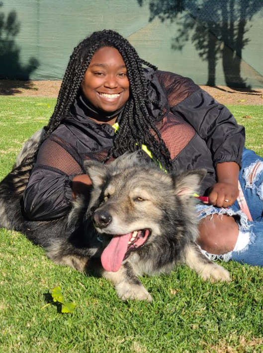 A woman is laying on the grass with a dog.