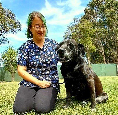 A woman with green hair is kneeling next to a black dog
