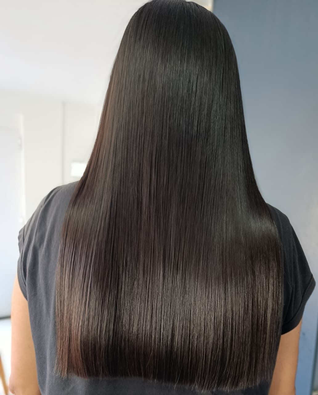 Persona de espaldas con cabello castaño oscuro, liso y brillante hasta la cintura.