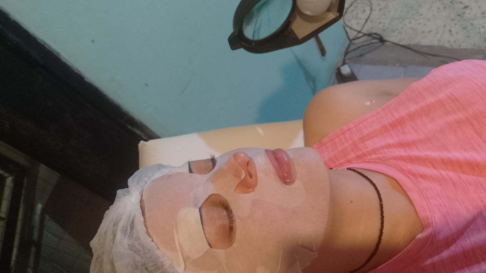 Persona recibiendo un tratamiento facial con mascarilla. Está tumbada bajo una lámpara de aumento.