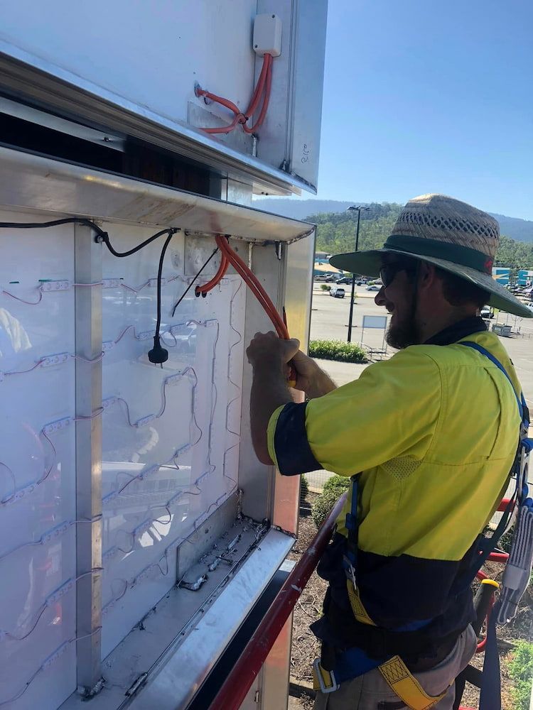 A Man In A Yellow Shirt And Hat Is Working On A Sign — Reef Electrical in Cannonvale, QLD