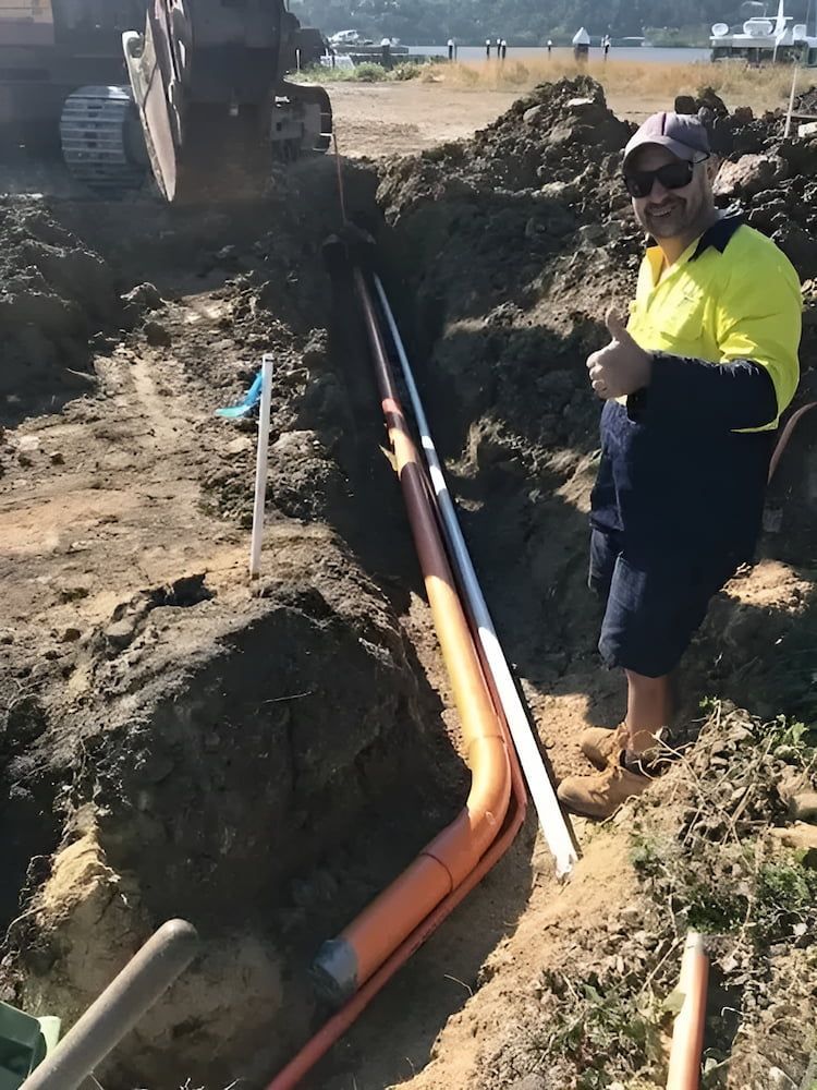 A Man Is Standing In The Dirt Next To A Pipe — Reef Electrical in Cannonvale, QLD