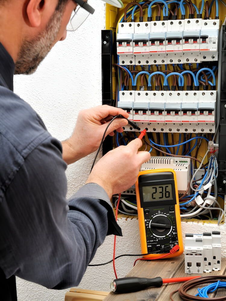 A Man Is Working On An Electrical Box With A Multimeter — Reef Electrical in Cannonvale, QLD
