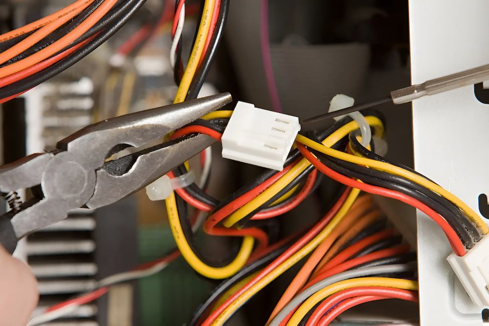 A Person Is Working On A Computer With A Pair Of Pliers — Reef Electrical in Cannonvale, QLD