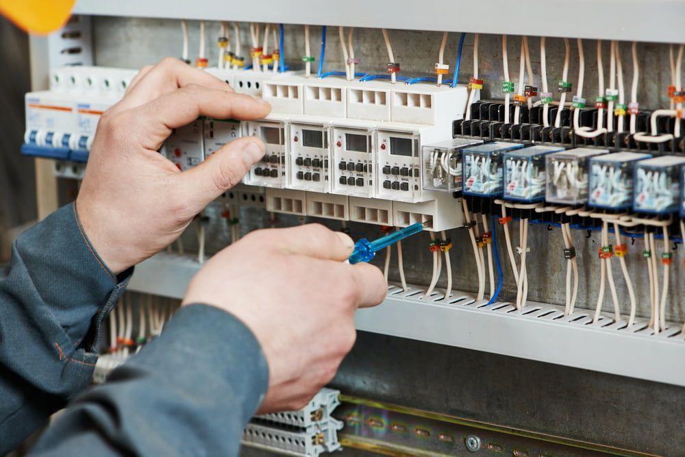 A Man Is Working On An Electrical Panel With A Screwdriver — Reef Electrical in Proserpine, QLD