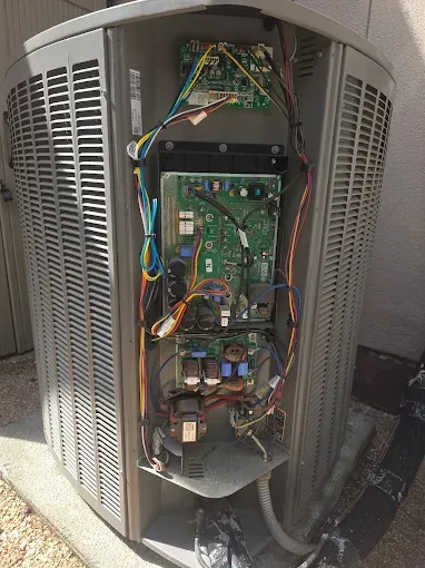 Open HVAC unit with exposed circuit boards, wiring, and components inside the outdoor cabinet