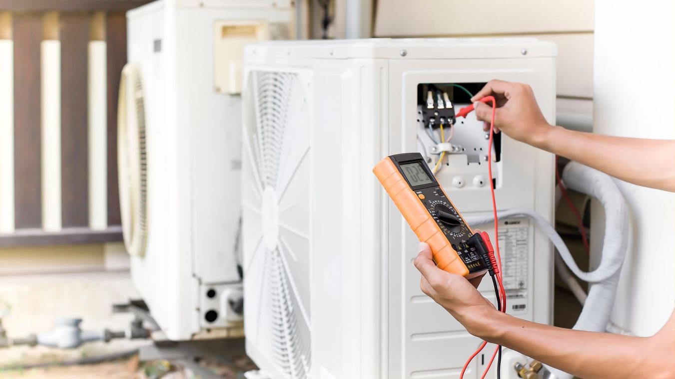 Technician testing an outdoor air conditioner unit with a multimeter and screwdriver
