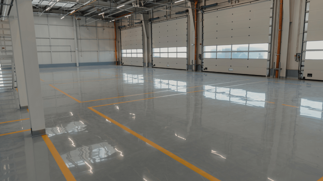 Wide view of a warehouse with a glossy, seamless epoxy floor reflecting light after an epoxy flooring service in Glendale, AZ