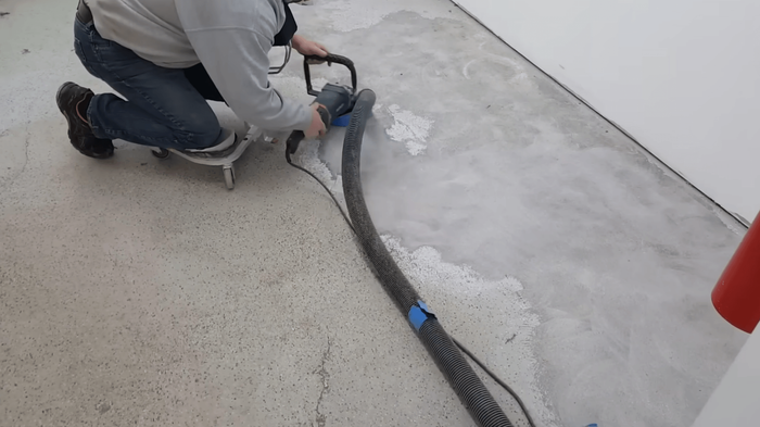 Worker using a floor grinder connected to a vacuum hose to prepare a concrete surface before coating during an epoxy flooring service in Glendale, AZ
