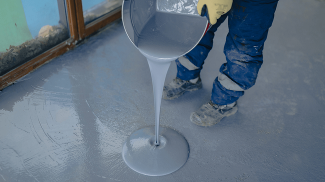 Worker pouring smooth liquid epoxy onto a concrete floor, creating a glossy base layer during an epoxy flooring service in Glendale, AZ