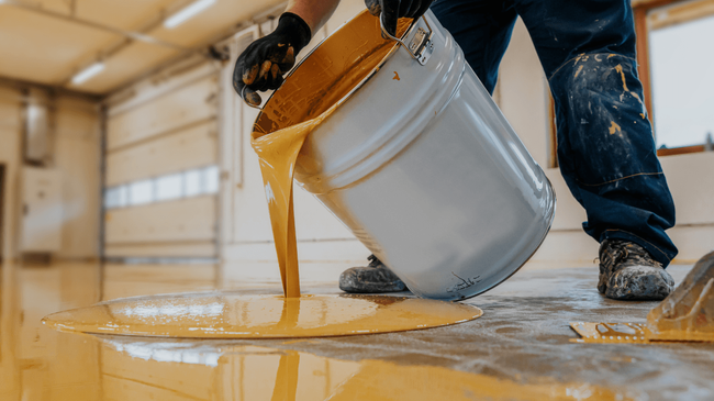 Worker pouring thick epoxy from a bucket and spreading it evenly across the floor during an epoxy flooring service in Glendale, AZ