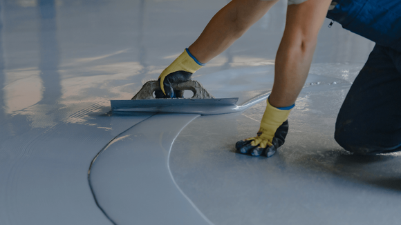Worker using a trowel to spread and level epoxy coating into a smooth finish during an epoxy flooring service in Glendale, AZ