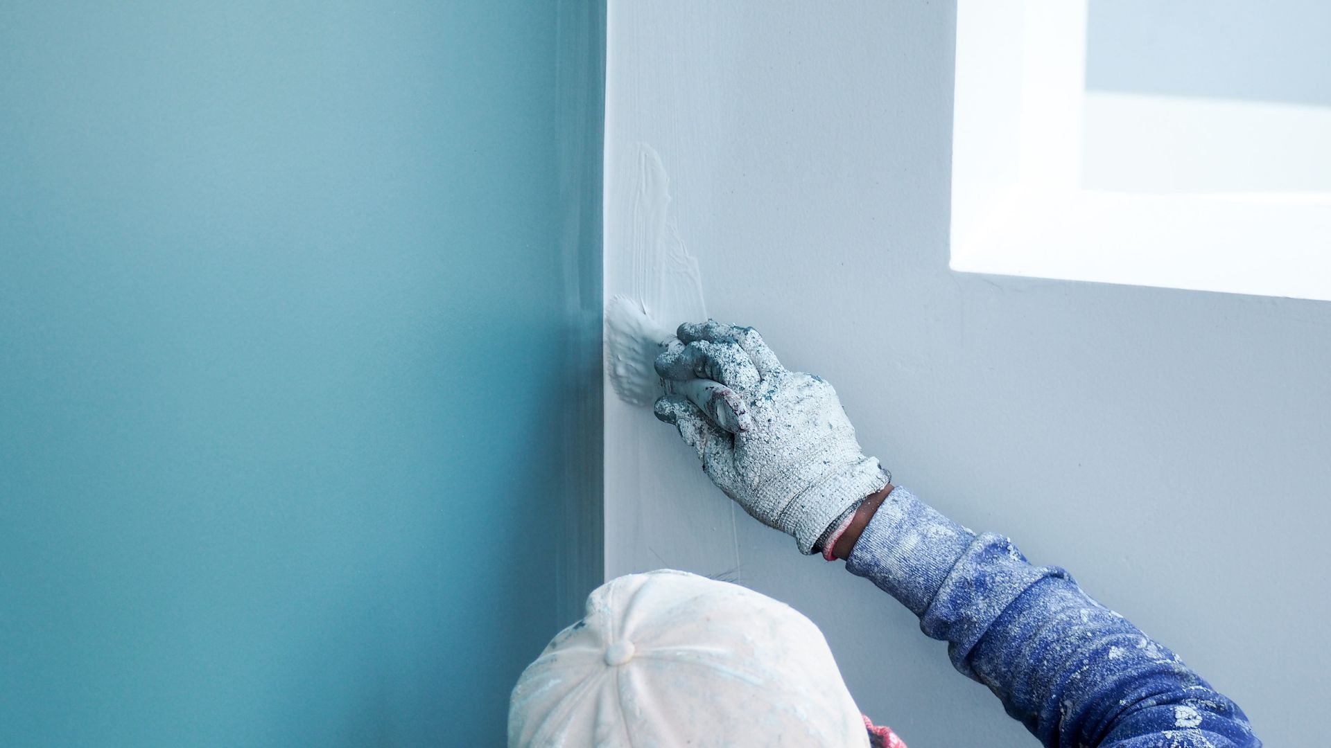 A worker paints the walls of a home with blue and white paint while using a brush.