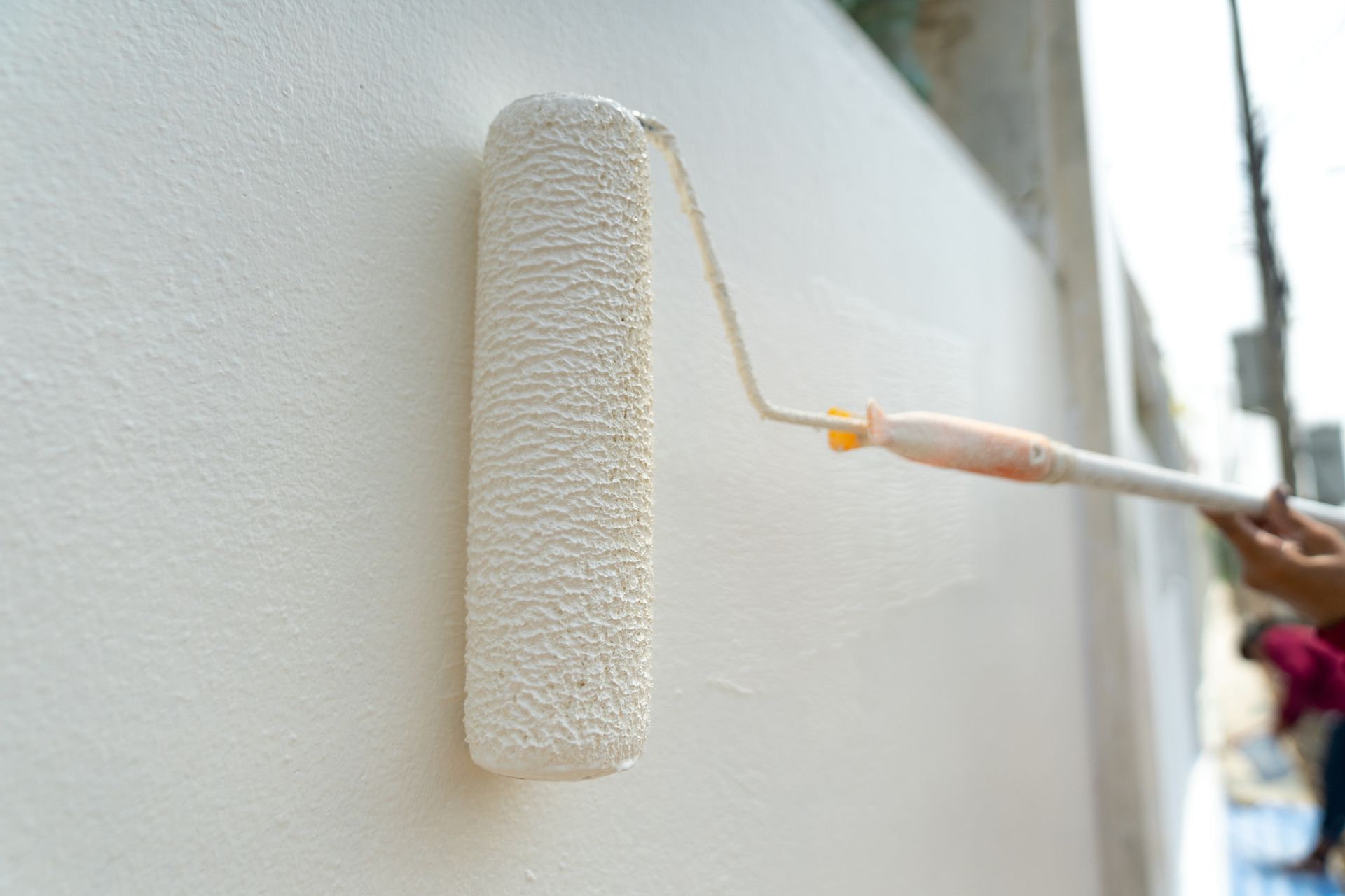 Close-up of a paint roller applying white paint to a wall.