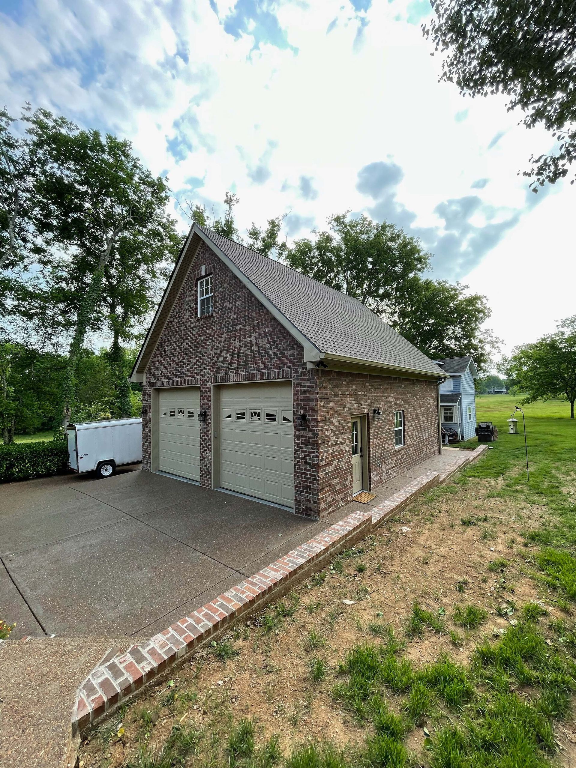 A brick garage with two garage doors is sitting in the middle of a grassy field.