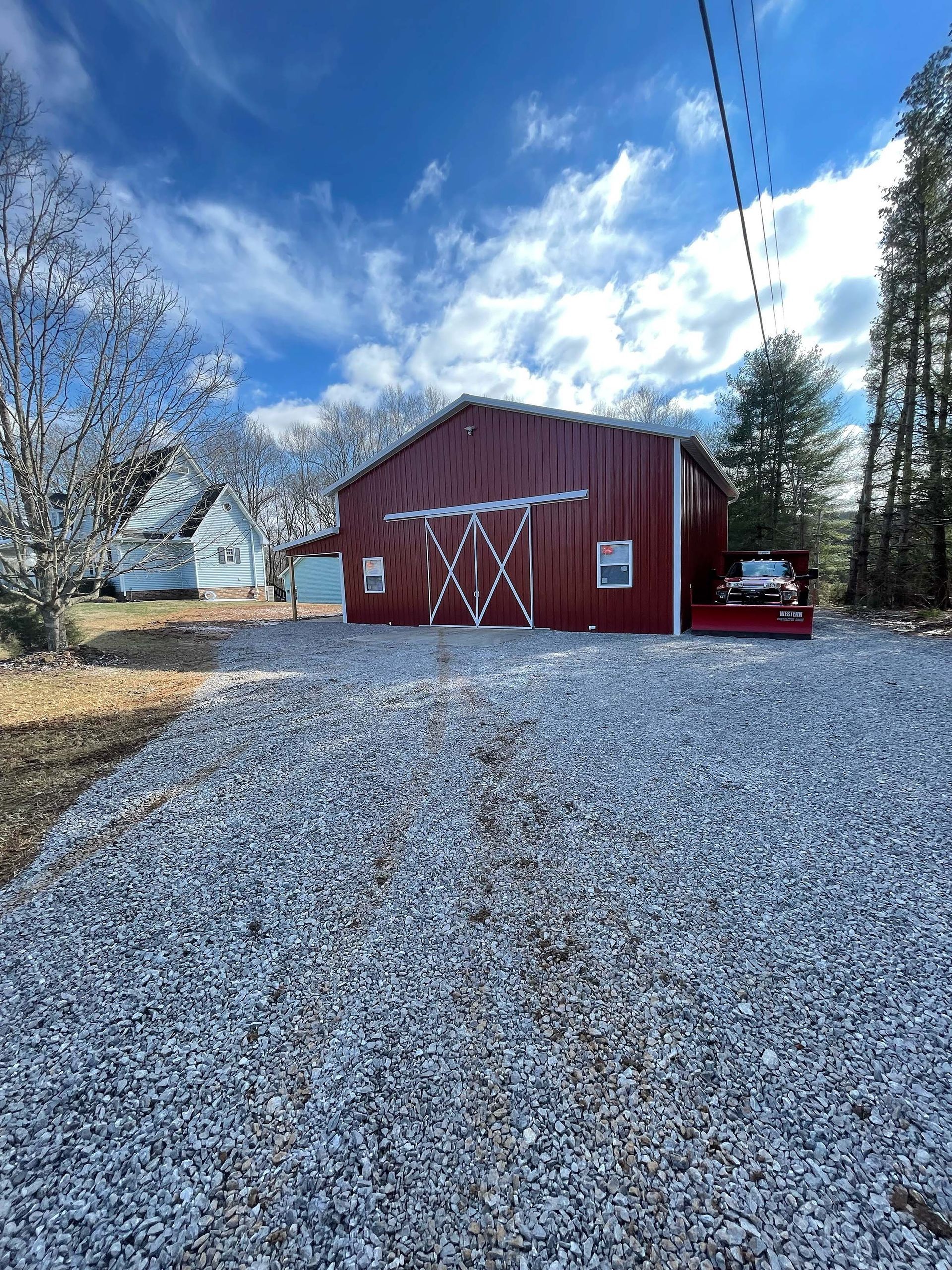 A red barn is sitting on top of a gravel driveway.