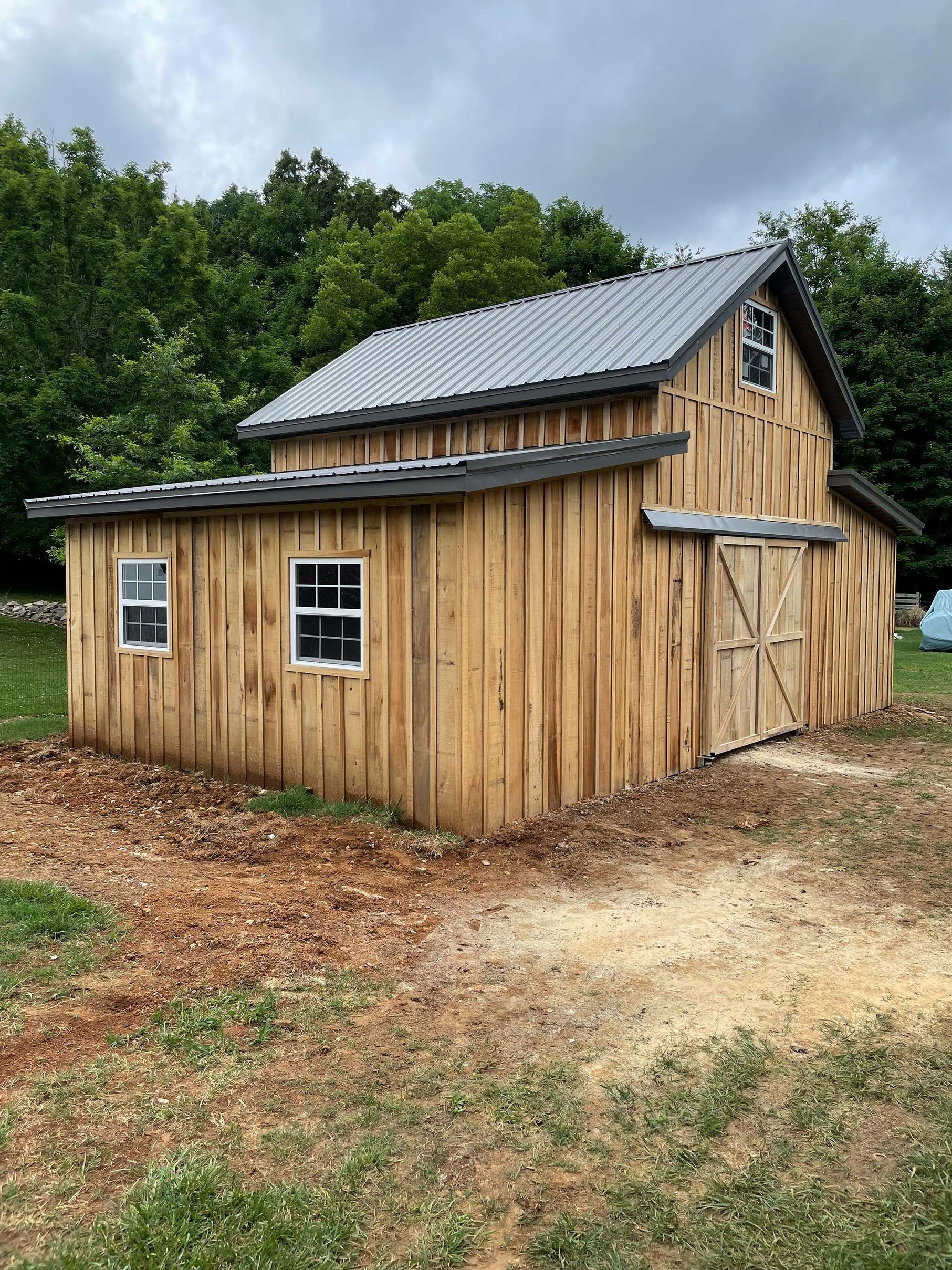 A wooden barn with a metal roof is sitting in the middle of a field.
