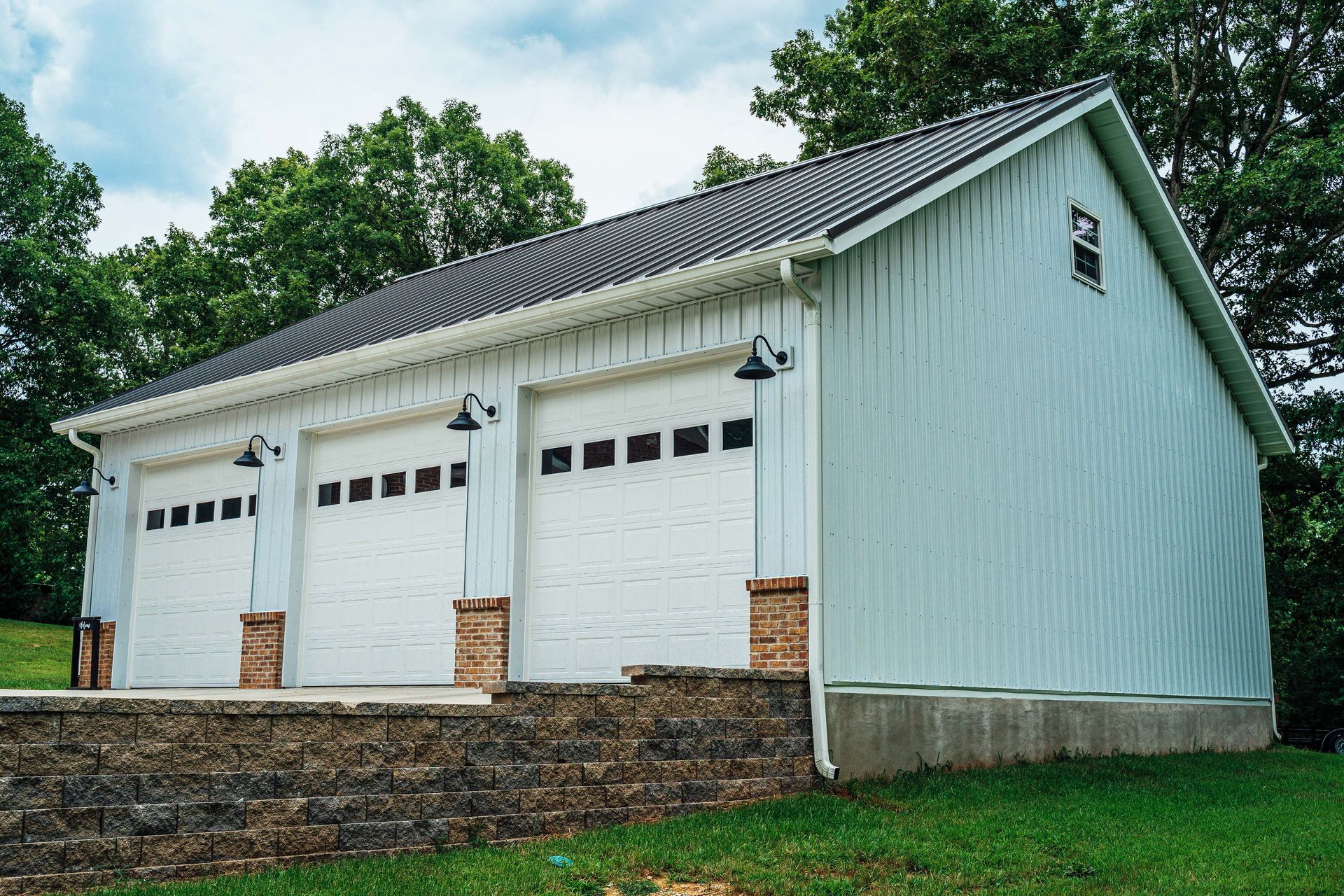 A white garage with three garage doors is sitting on top of a lush green field.