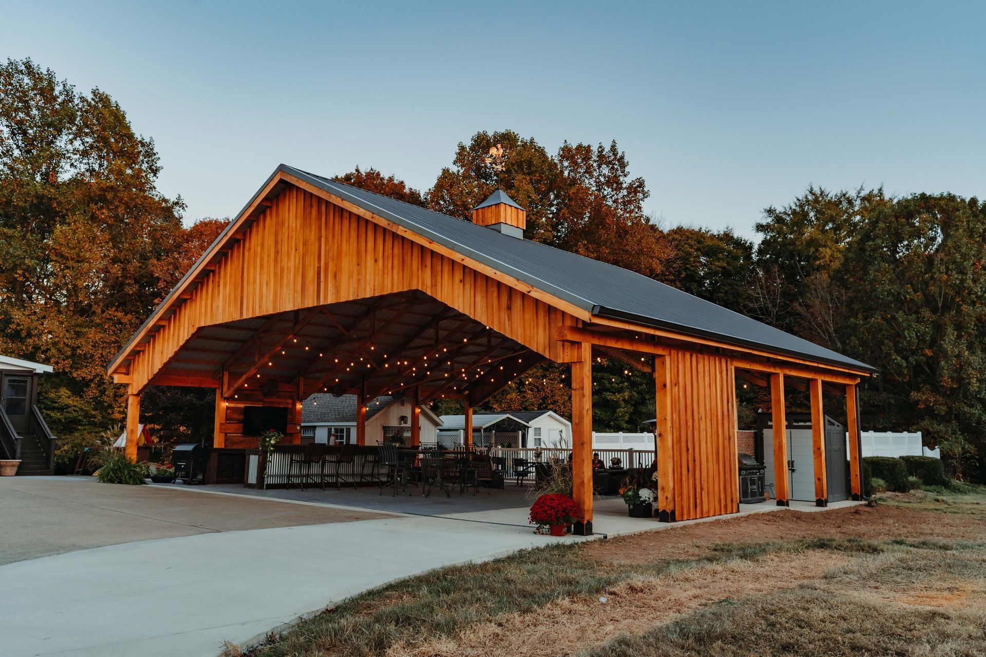 A large wooden pavilion with a metal roof is surrounded by trees.
