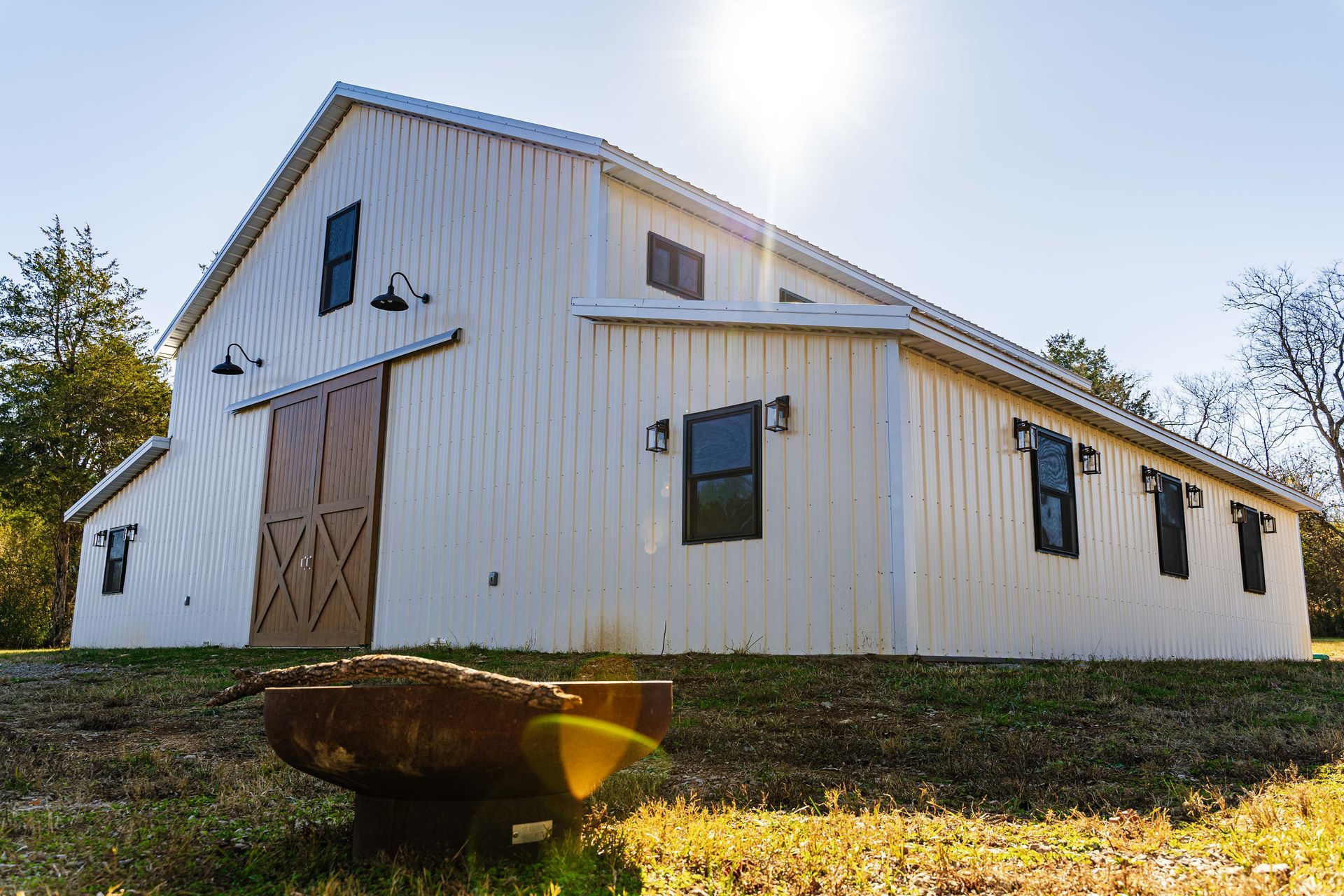 A large white barn is sitting on top of a grassy hill.
