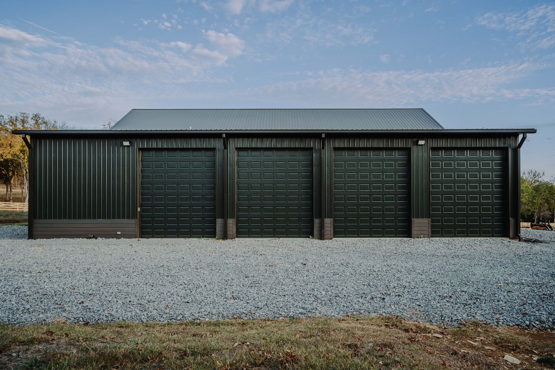 A large black garage with three garage doors is sitting on top of a gravel driveway.