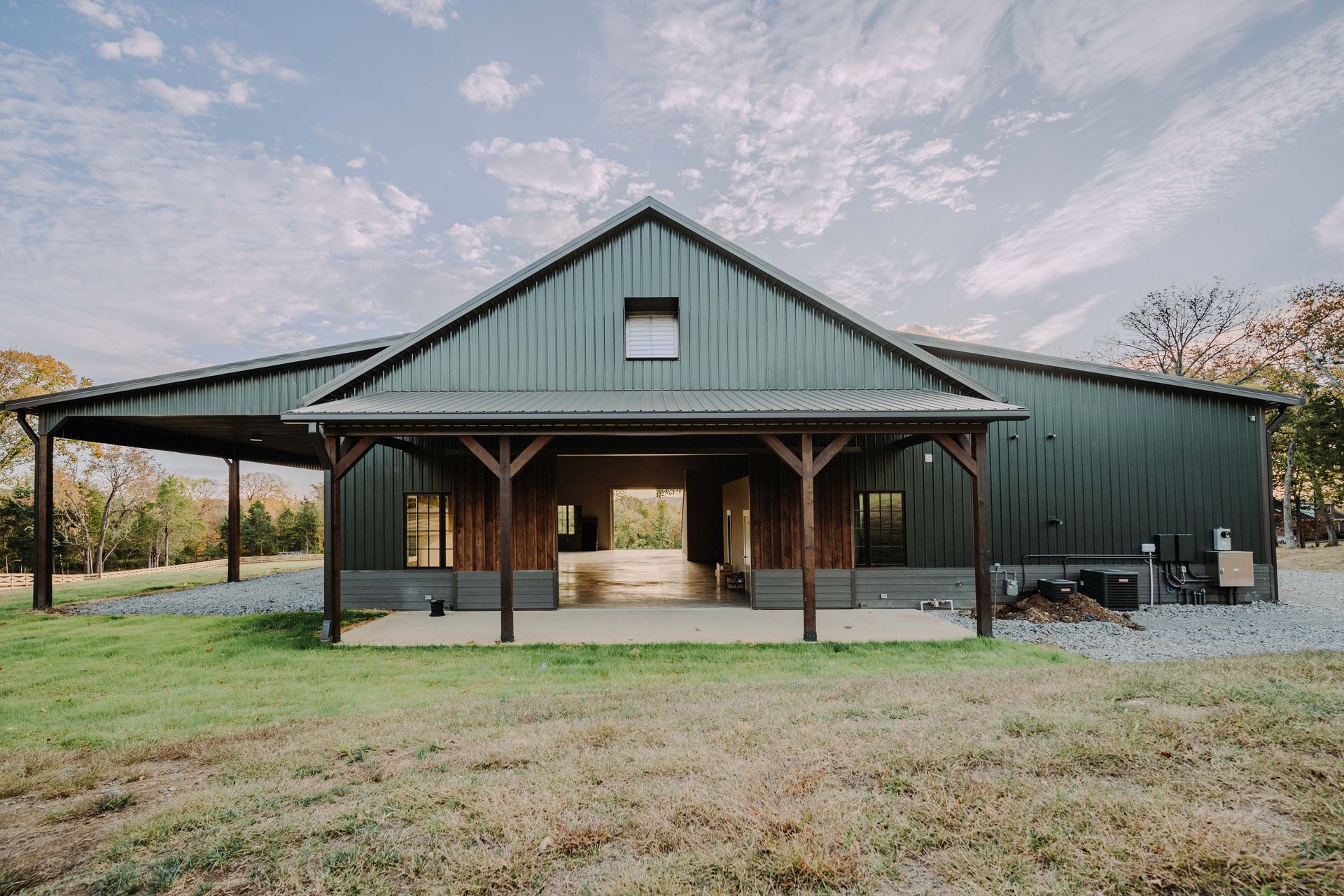 A large green barn with a porch in the middle of a field.