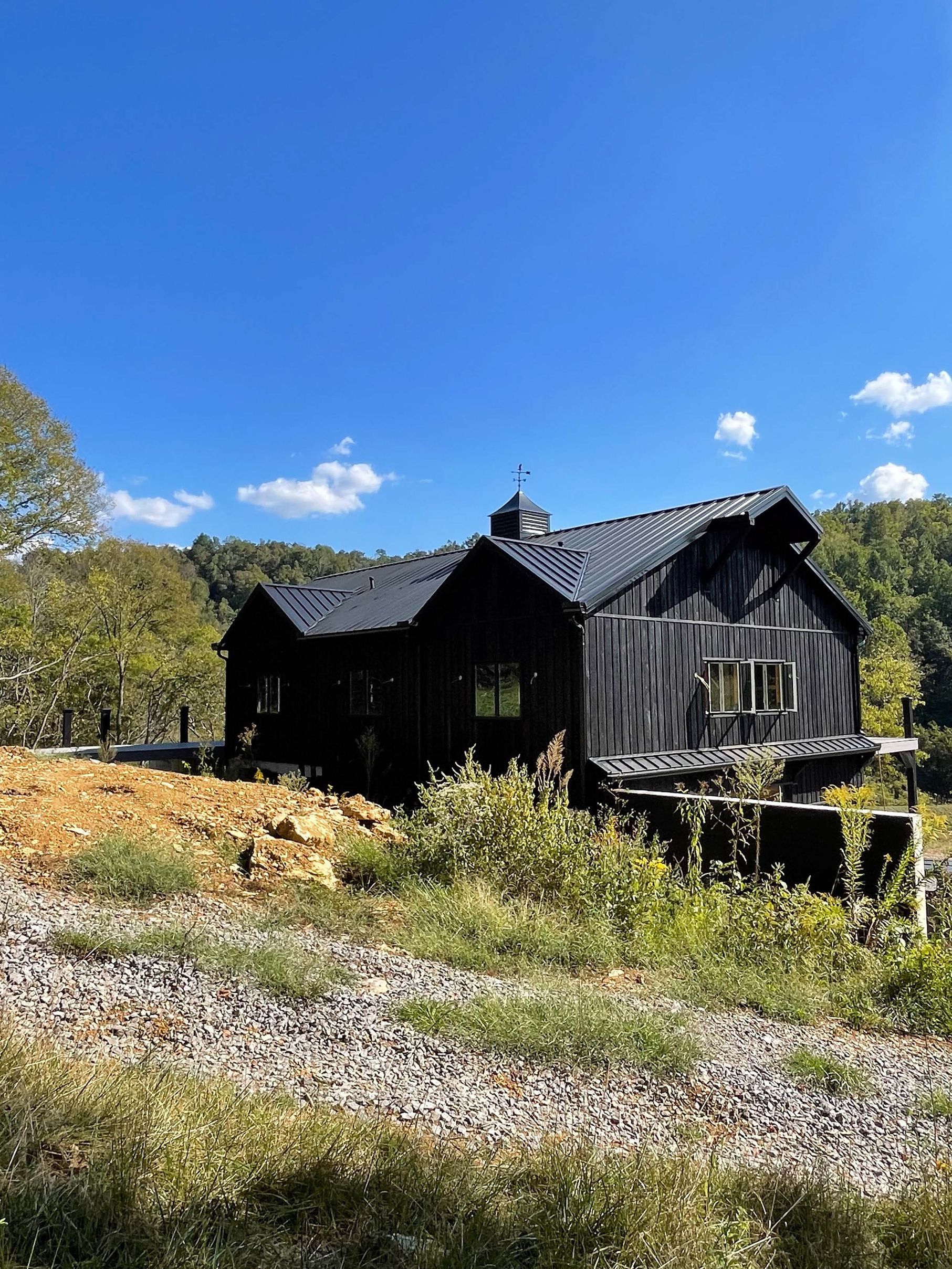 A large black house is sitting in the middle of a field.